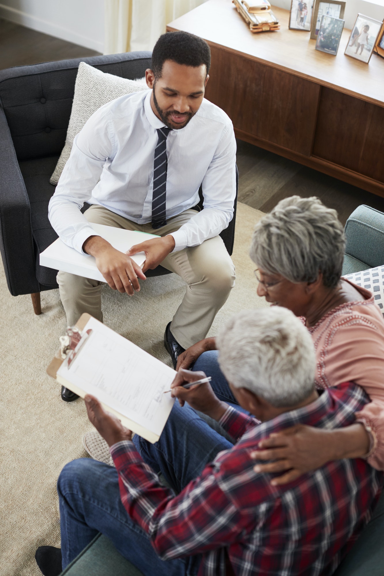 Senior Couple Meeting With Male Financial Advisor At Home And Signing Document